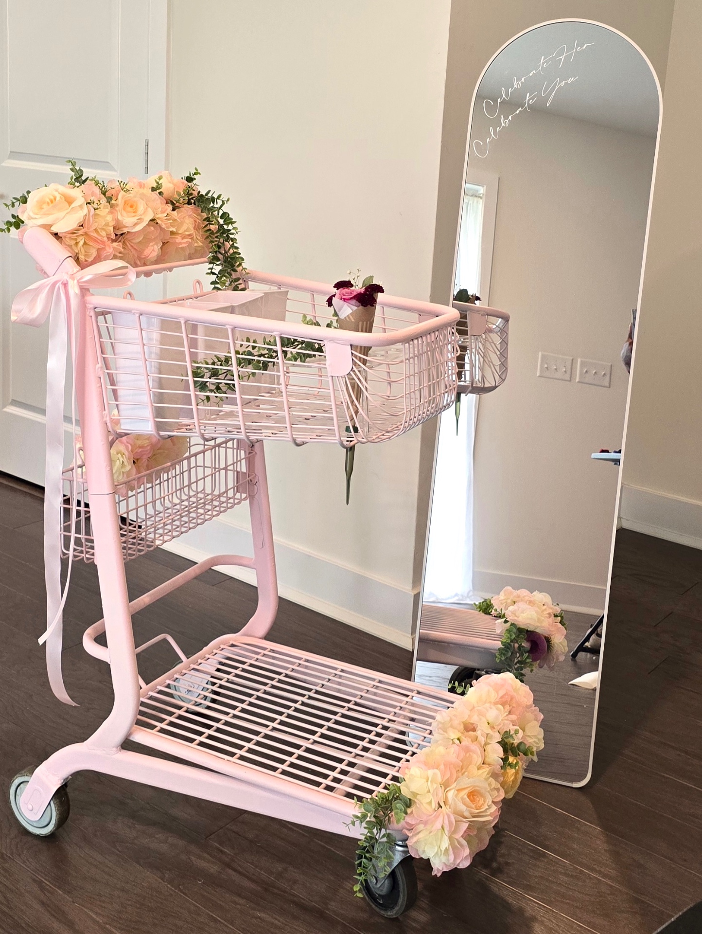 Hand-painted dusty pink floral cart with cascading roses, eucalyptus and a satin ribbon, beside an arched mirror